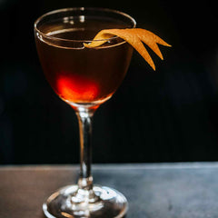 Bijou cocktail on bar in front of dark background with orange twist