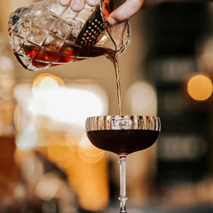 Black Manhattan cocktail, bartender pouring into cocktail glass through strainer