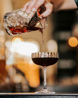 Black Manhattan cocktail, bartender pouring into cocktail glass through strainer