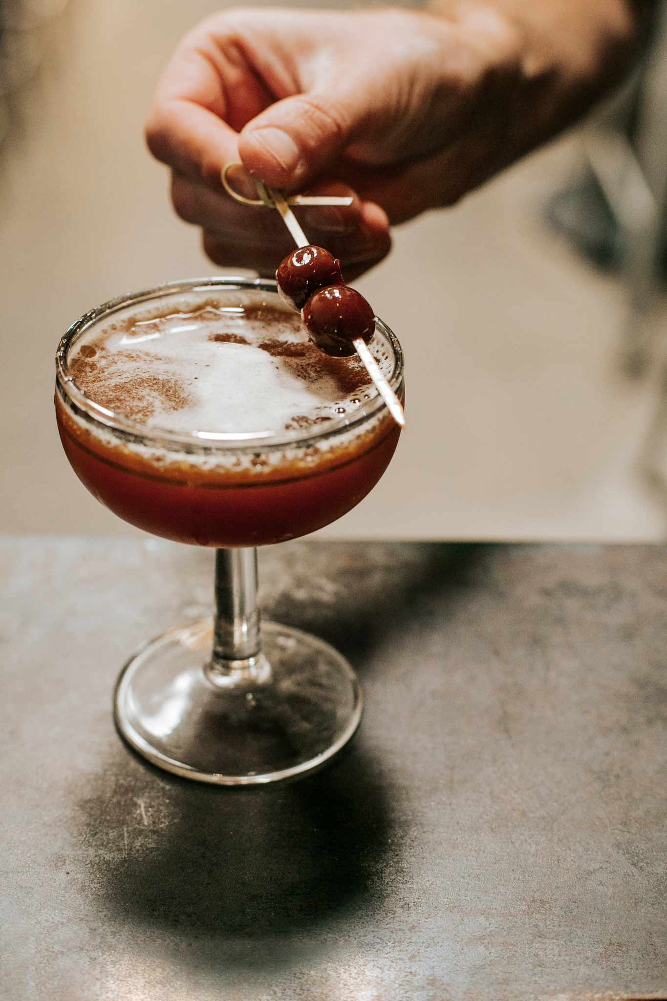 Blood and Sand cocktail with hand placing cherries