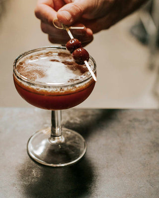 Blood and Sand cocktail with hand placing cherries