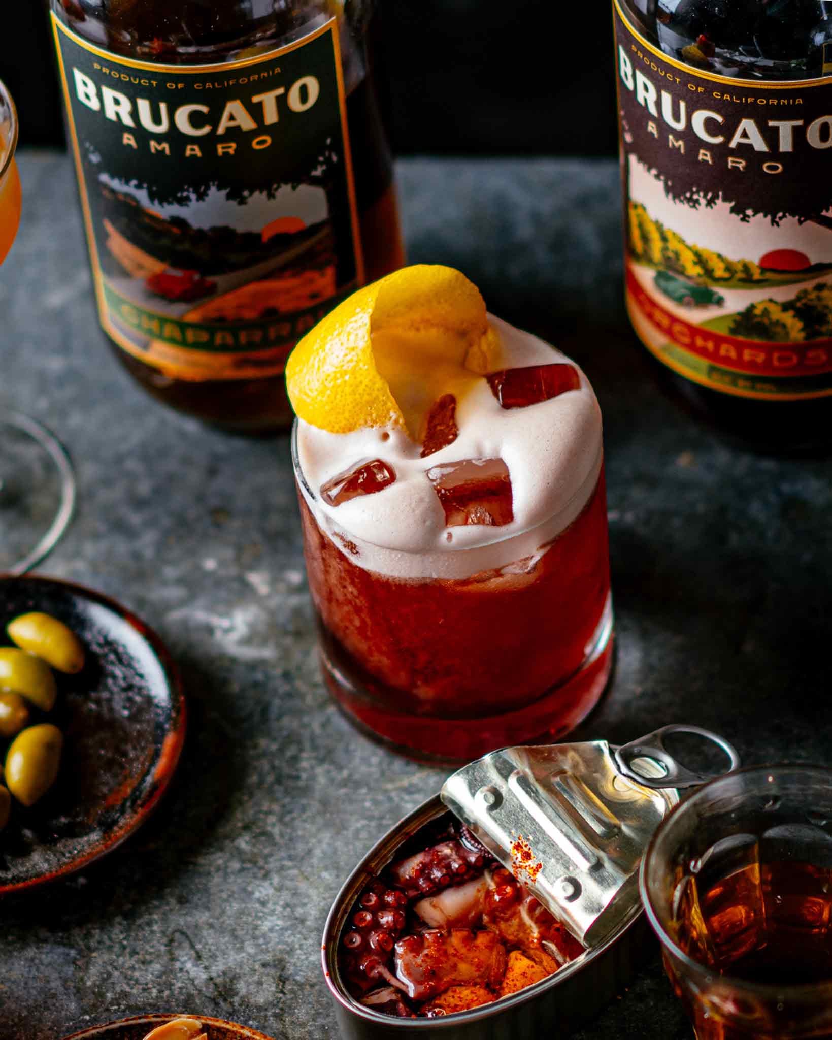 Fiddler's Green cocktail with orange twist in front of Brucato Amaro Bottles