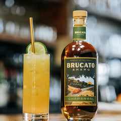 Gamboa Beach cocktail with straw next to bottle of Brucato Amaro Chaparral on bar