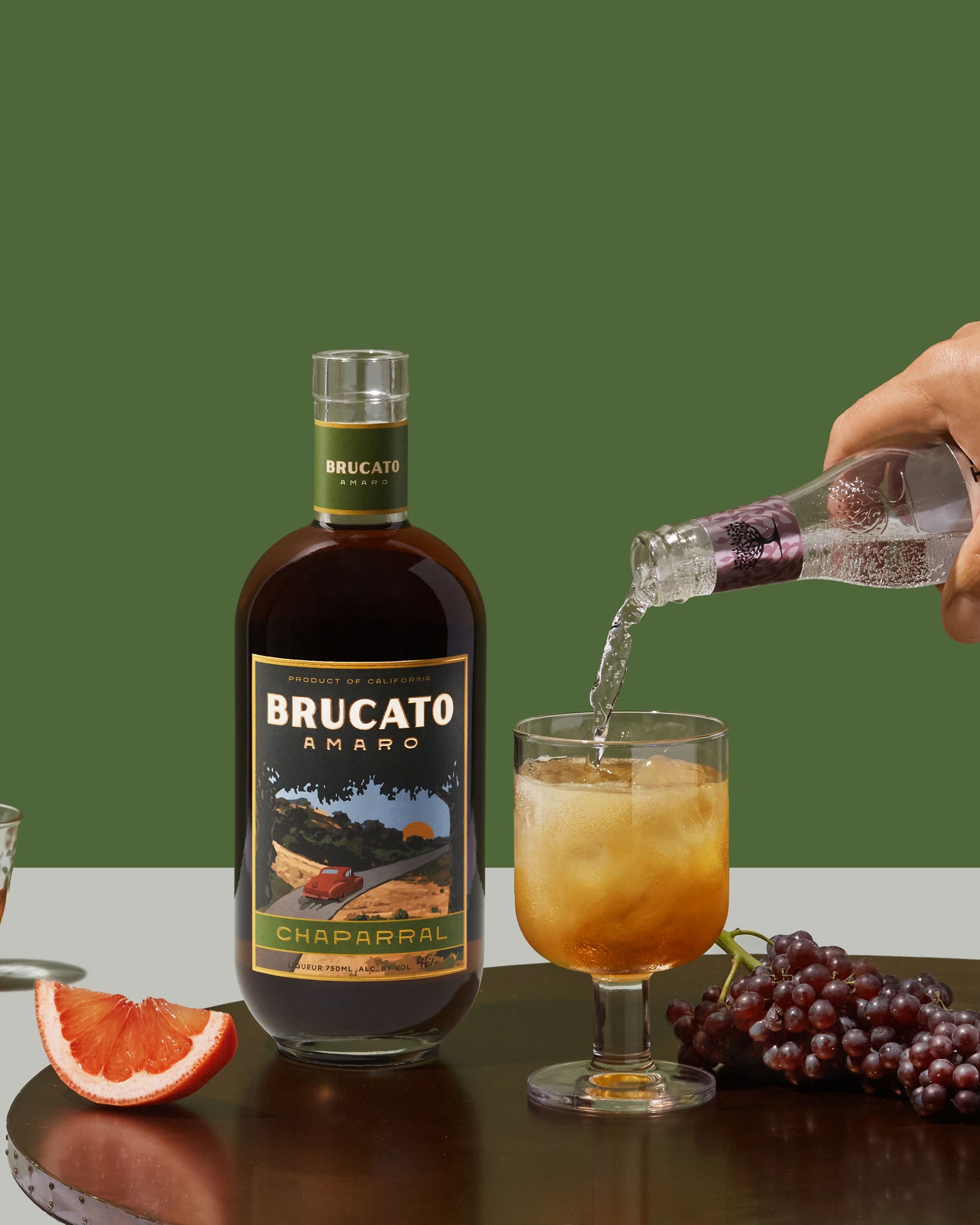 hand pouring soda water into highball cocktail in front of Brucato Amaro Chaparral bottle