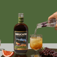 hand pouring soda water into highball cocktail in front of Brucato Amaro Chaparral bottle