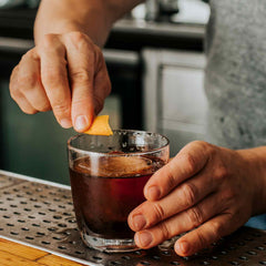 Junction House cocktail in glass with bartender adding orange twist