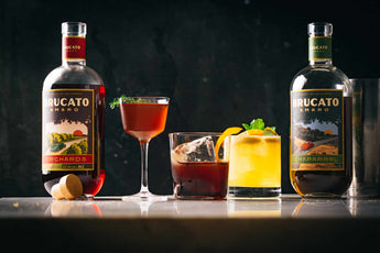 Brucato Amaro Bottles and cocktails on a table with a dark background