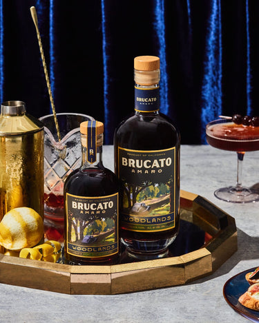 Brucato Amaro Woodlands bottles, cocktails, and food on a decorated table.